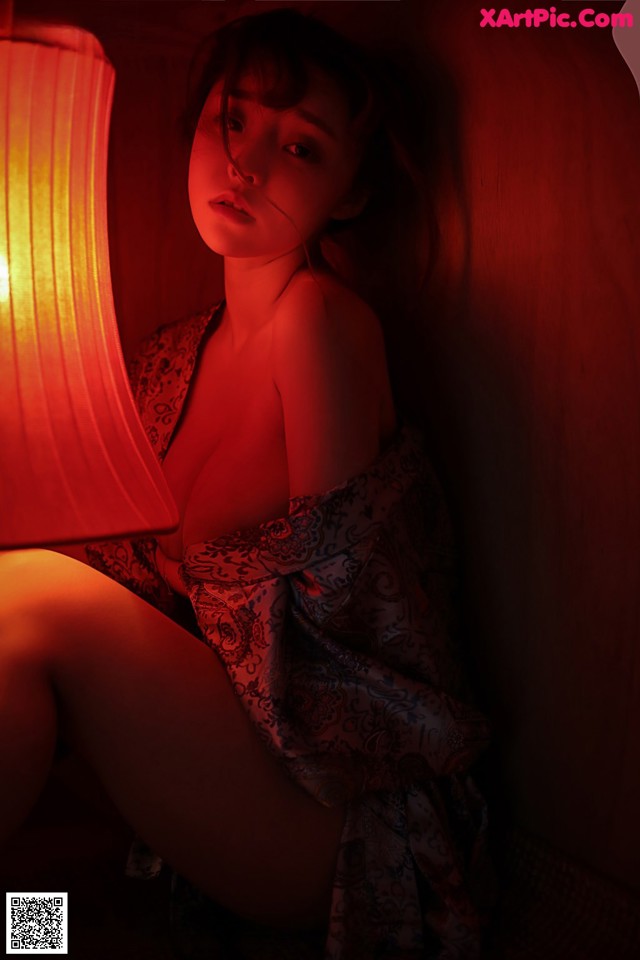 A woman sitting under a red lamp in a room.