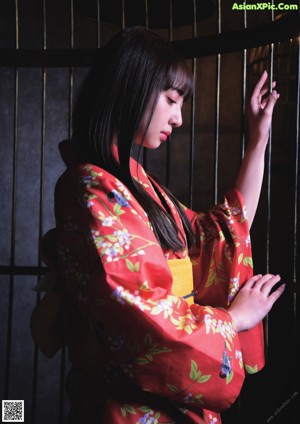 A woman in a red kimono standing in front of a cage.