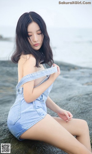 A woman sitting on a rock by the ocean.