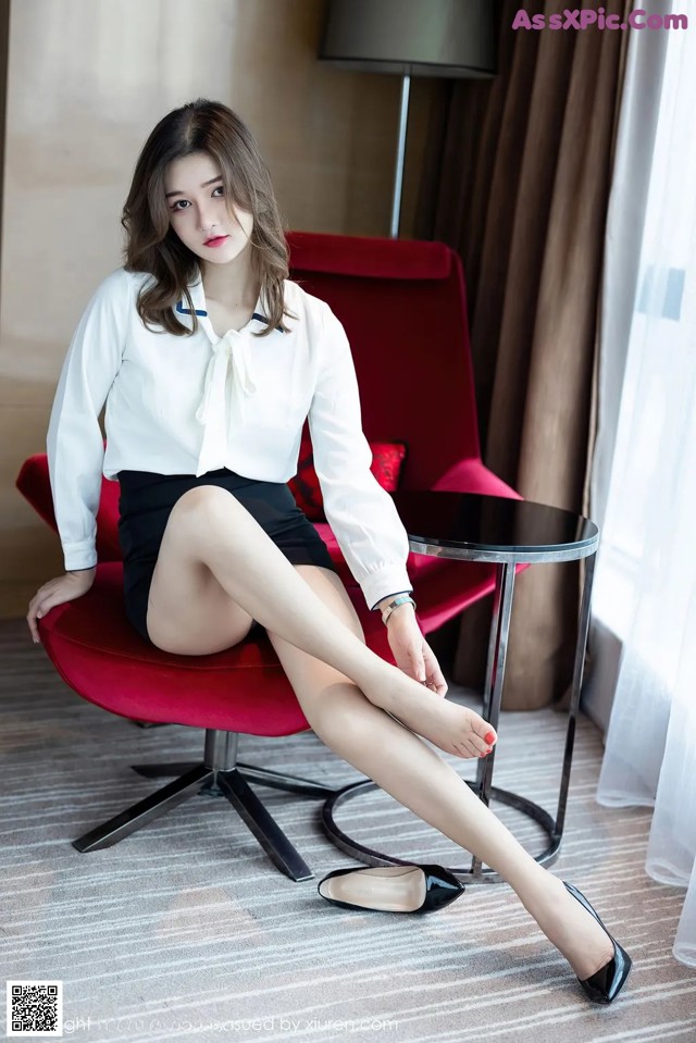 A woman sitting on a red chair with her legs crossed.