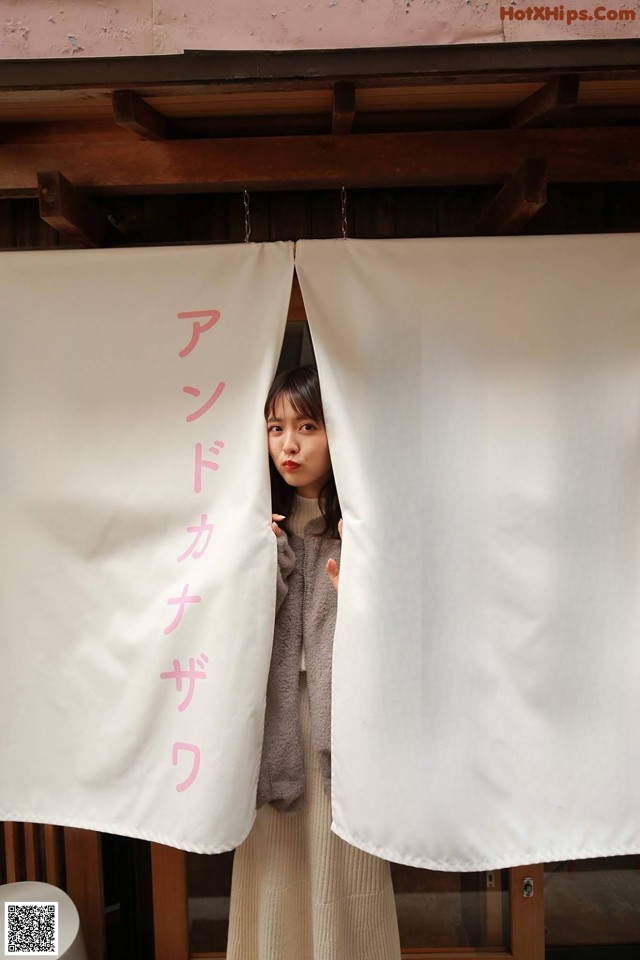 A woman standing in front of a white curtain with pink writing.