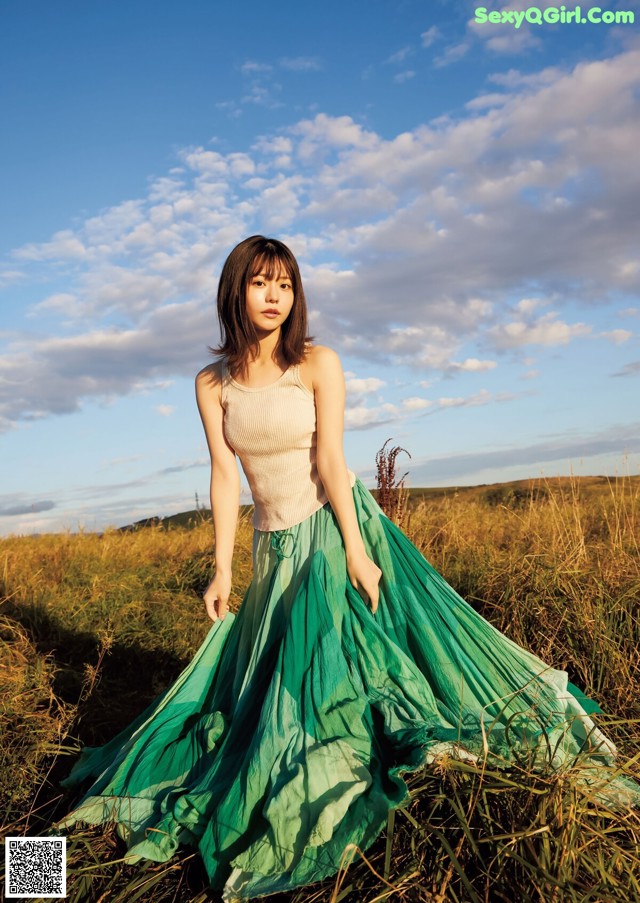 A woman in a long green skirt standing in a field.