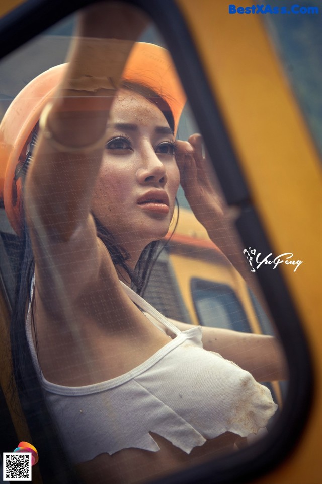 A woman wearing a hard hat looking out the window of a car.