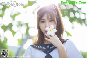 A woman in a school uniform leaning against a tree.