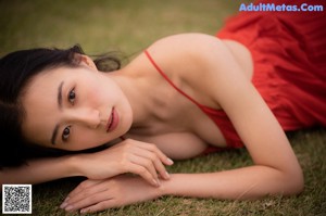 A woman in a red dress sitting on a dirt road.