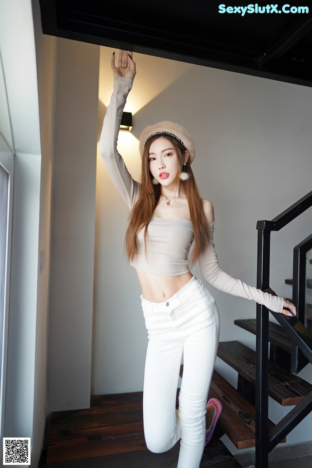 A woman in white pants and a beige top posing for a picture.