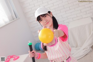 A woman in a pink shirt and striped shorts holding a green ball.