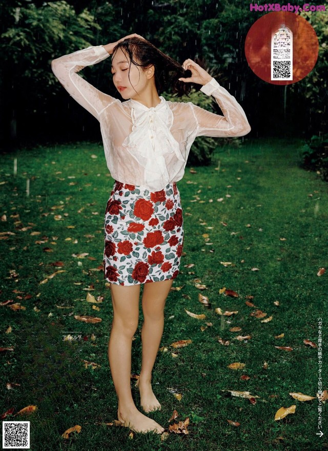 A woman in a white blouse and floral skirt standing in the grass.