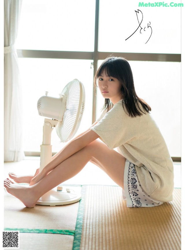 A woman sitting on the floor next to a fan.