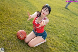 A woman sitting on the grass with a basketball.