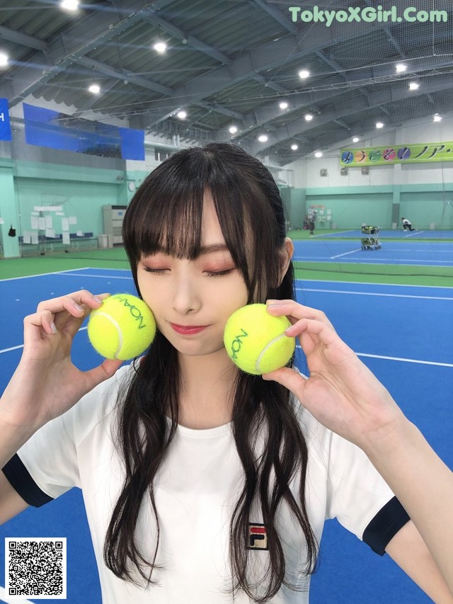 A woman holding two tennis balls in front of her face.