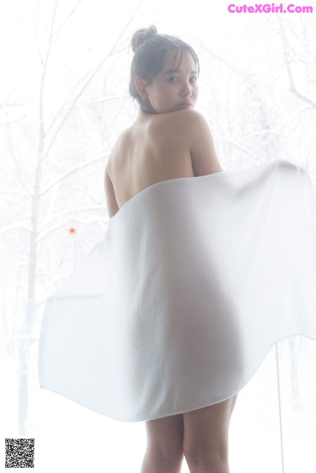 A woman in a white dress standing in front of a window.