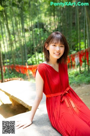 A woman in a floral dress leaning against a wall.