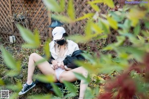 A woman wearing a black jacket and a face mask standing in a garden.