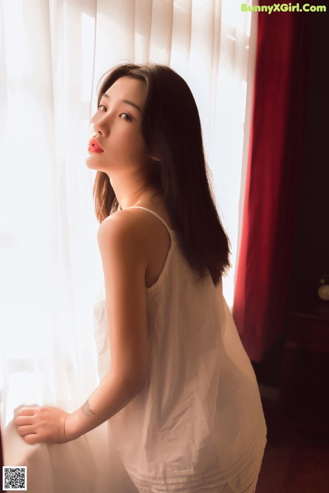 A woman in a white dress leaning against a window.